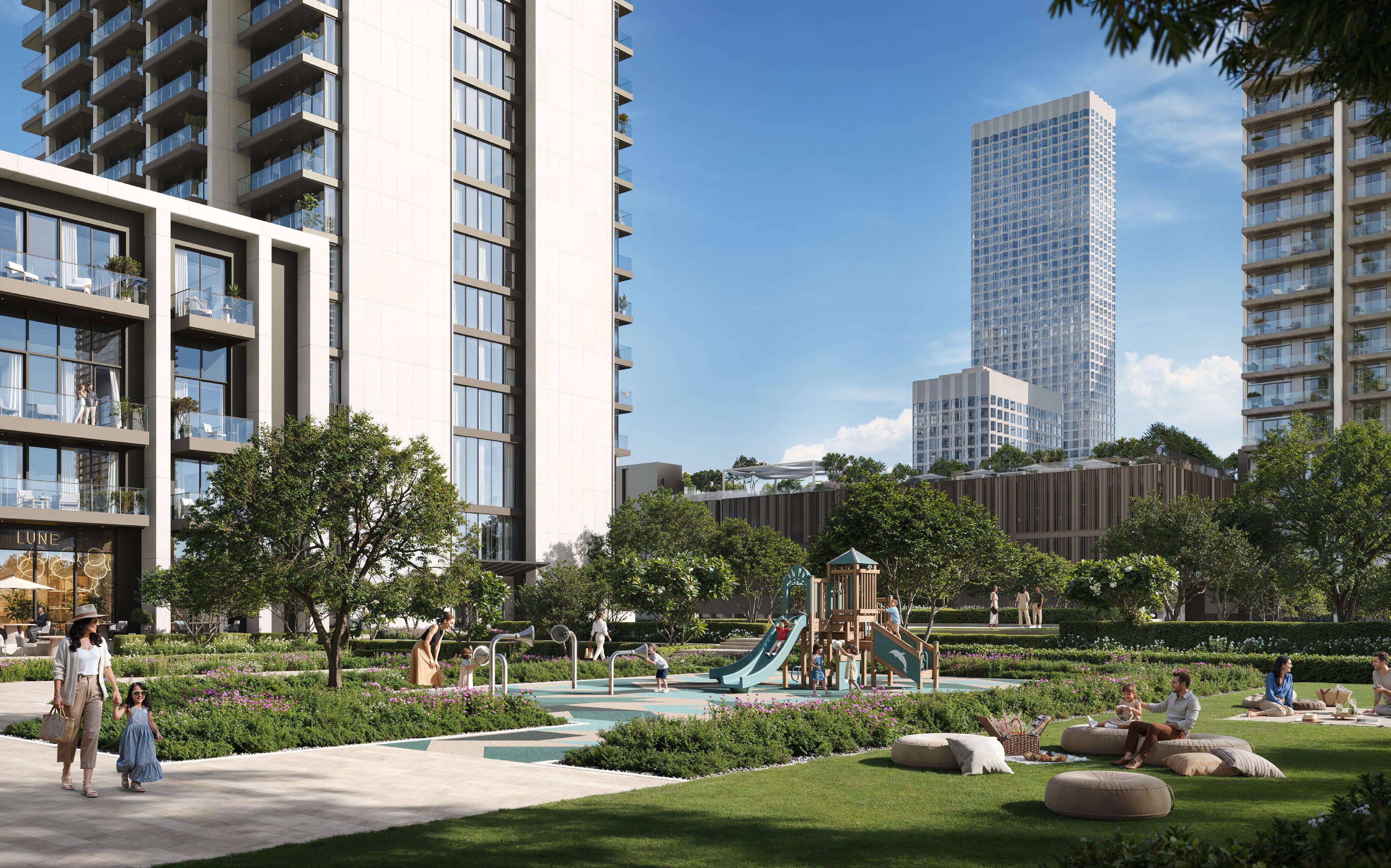 Families in a sunny garden with a playground and picnic lawn below the towers